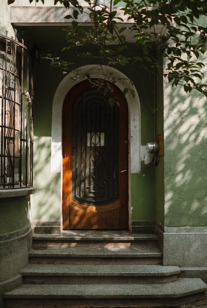Warm sunlight on vintage green facade with arched wooden door, suggesting an artistic urban design.